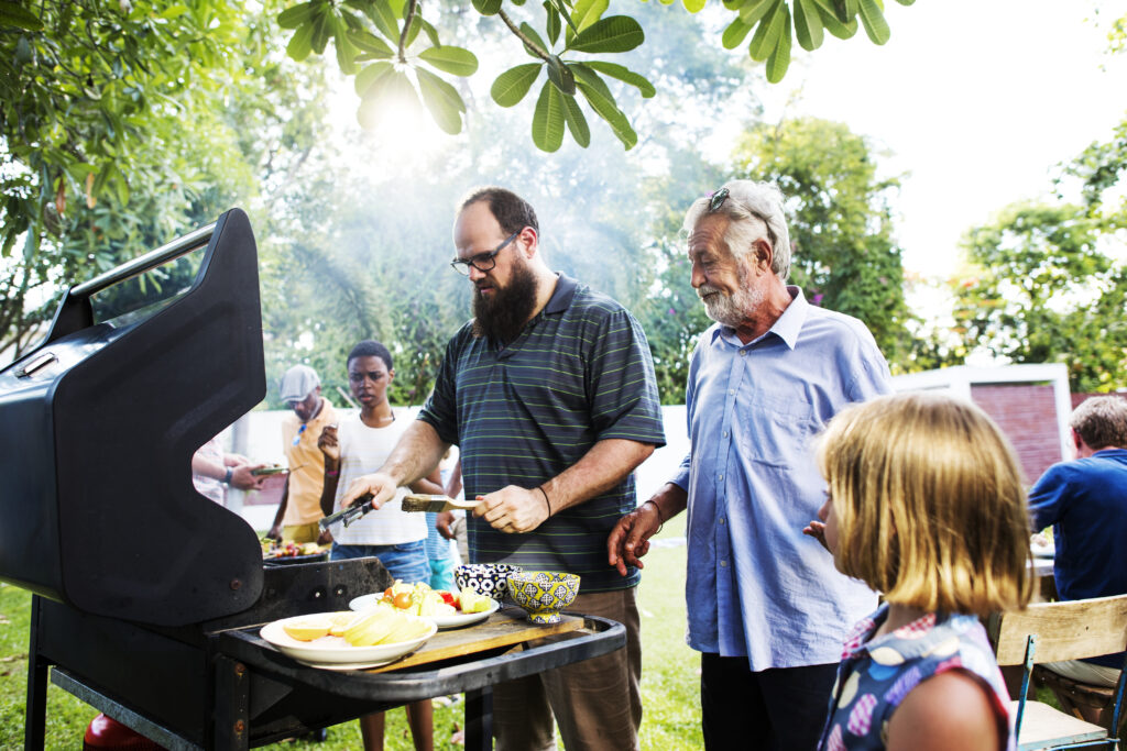 BBQ brings people together. A community of diverse people and families get together to prepare and cook a barbecue.